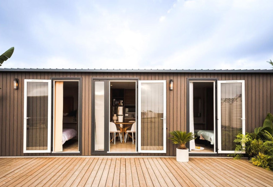Lujosa cabaña moderna con grandes puertas de cristal, terraza de madera y vegetación tropical alrededor.