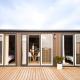 Moderne luksuslodge med store glasdøre, træterrasse og omgivet af tropiske planter under himlen.