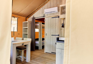 Interieurzicht van safaritent Villatent Outback met eettafel, stapelbed en airco aan de muur.