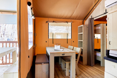 Interior de una tienda safari Villatent Outback con mesa de comedor, sillas y literas de madera clara.