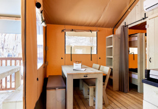 Intérieur d'une tente safari Villatent Outback avec table à manger, bancs et lits superposés en bois.