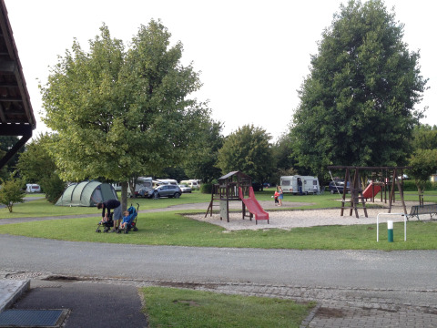 Parque de vacaciones con zona de juegos, tiendas, caravanas y familias en un entorno verde en Francia.