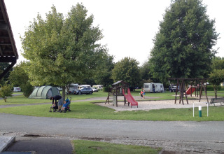 Campingplads med legeplads, telte, campingvogne og familier, træer og åbne grønne områder i Frankrig.