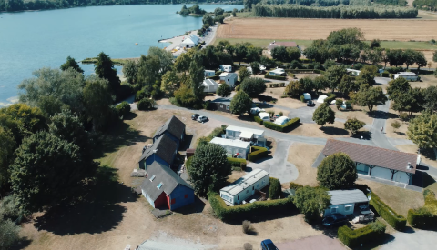 Luftaufnahme des Camping Seasonova Les Marguerites in Hauts-de-France mit See, Hütten und Caravan.