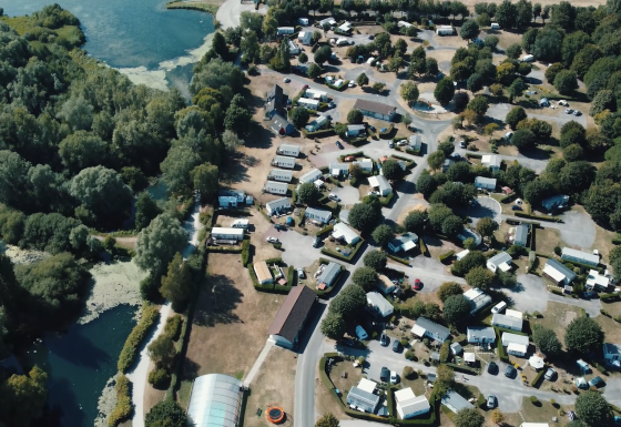 Luftfoto af Camping Seasonova Les Marguerites i Hauts-de-France, Frankrig, omgivet af træer og søer.