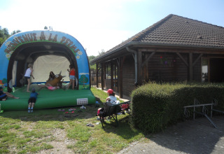 Børn leger på en oppustelig hoppeborg ved siden af en træbygning i Camping Seasonova Les Marguerites, Frankrig.