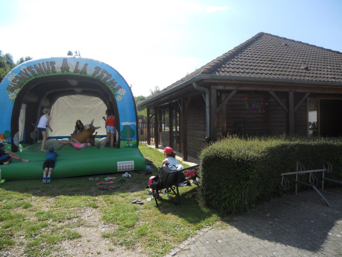 Kinderen spelen op een springkussen naast een houten gebouw op Camping Seasonova Les Marguerites, Frankrijk.