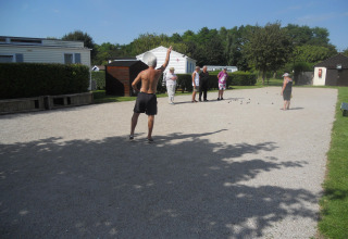 Persone giocano a pétanque su un campo di ghiaia al sole al Camping Seasonova Les Marguerites, Hauts-de-France, Francia.