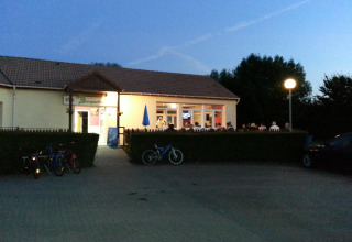 Aftenbillede af et oplyst fælleshus med gæster ved Camping Seasonova Les Marguerites i Hauts-de-France.