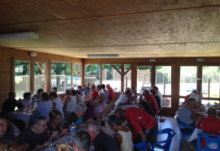 En gruppe mennesker sidder sammen og spiser indendørs på Camping Seasonova Les Marguerites i Hauts-de-France.