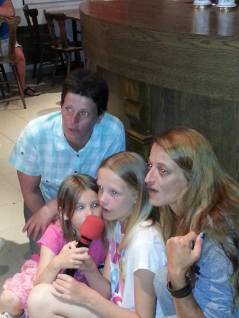 Two women and two girls sit together holding a red microphone at Camping Seasonova Les Marguerites holiday park in France.