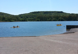 Vista di un lago con colline sullo sfondo e persone su pedalò gialli al Camping Seasonova Les Marguerites.