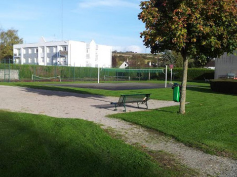 Zona exterior en Camping Seasonova Les Marguerites, Hauts-de-France, con césped verde, banco y cancha de tenis.