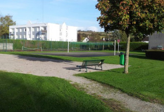 Area esterna a Camping Seasonova Les Marguerites, Hauts-de-France, con panchina, prato verde e campo da tennis.