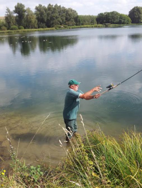 Hombre pescando en el lago en Camping Seasonova Les Marguerites, Hauts-de-France, rodeado de naturaleza.