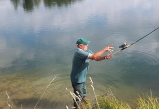Homme pêchant au bord du lac au Camping Seasonova Les Marguerites, Hauts-de-France, entouré de nature.