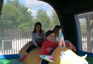 Children play on an inflatable animal-shaped bouncer at a holiday park, sunlight streaming inside.