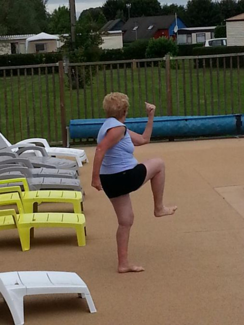 Ältere Frau in Sportkleidung macht eine Übung am Pool im Camping Seasonova Les Marguerites, Hauts-de-France.