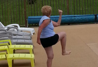 Oudere vrouw in sportieve outfit doet oefeningen aan het zwembad op Camping Seasonova Les Marguerites, Hauts-de-France.