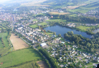Luftfoto af Camping Seasonova Les Marguerites feriepark og sø i det grønne landskab i Hauts-de-France.