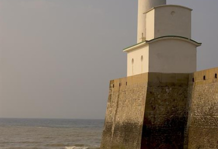 Faro en la costa cerca de Gamaches, Hauts-de-France, Francia, con personas sentadas en la playa rocosa.