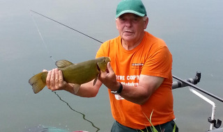 Hombre con camiseta naranja sostiene un pez junto al lago cerca de Gamaches, Hauts-de-France, Francia.