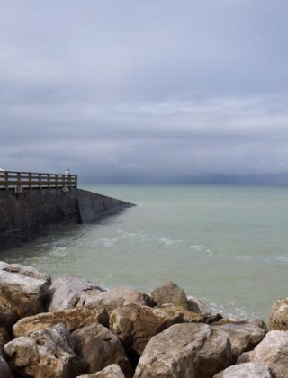 Vista costera cerca de Gamaches, Hauts-de-France, Francia, con rocas, un muelle y mar tranquilo bajo cielo nublado.