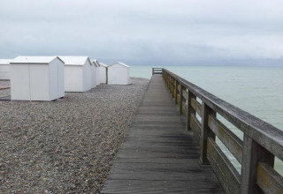 Passerella di legno sulla spiaggia di ciottoli con casette bianche a Camping Seasonova Les Marguerites, Hauts-de-France.