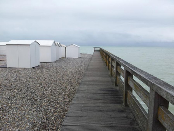 Houten promenade langs het kiezelstrand met witte huisjes bij Camping Seasonova Les Marguerites, Hauts-de-France.