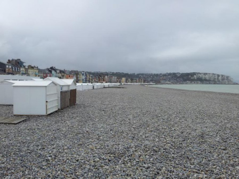 Stenstrand med hvide badehytter og farverige huse i baggrunden på Camping Seasonova Les Marguerites, Hauts-de-France.