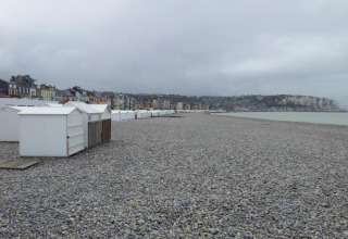Spiaggia di ciottoli con cabine bianche e case colorate al Camping Seasonova Les Marguerites, Hauts-de-France, Francia.
