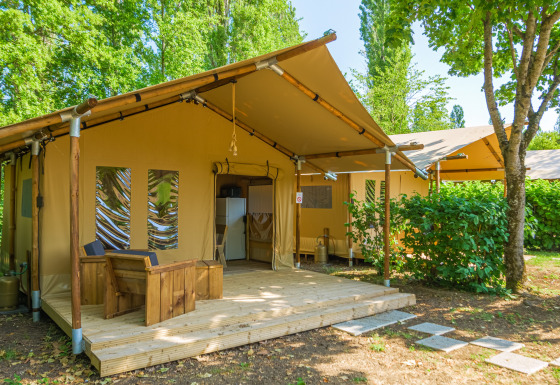 Image of a safari tent named Slow Lodge without bathroom facilities, surrounded by trees and greenery.
