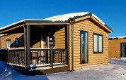 Cabaña de madera con techo cubierto de nieve y porche en Camping & Ferienpark Brilon, Alemania bajo cielo azul.