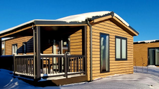 Baita in legno con tetto coperto di neve e veranda al Camping & Ferienpark Brilon, Germania, sotto cielo blu.