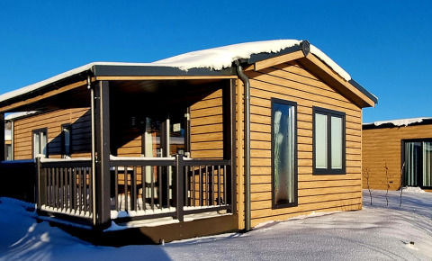 Cabaña de madera con techo cubierto de nieve y porche en Camping & Ferienpark Brilon, Alemania bajo cielo azul.
