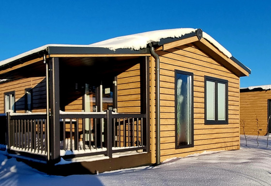 Cabaña de madera con techo cubierto de nieve y porche en Camping & Ferienpark Brilon, Alemania bajo cielo azul.