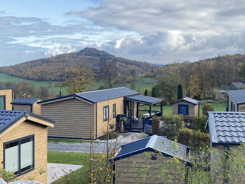 Chalet in legno al Camping & Ferienpark Brilon, Germania, con colline e foreste sullo sfondo.