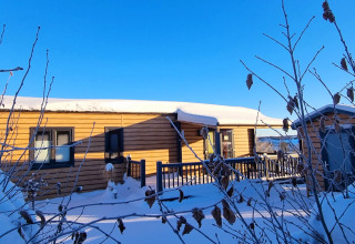 Cabaña de madera nevada en Chalet Waldfee, Camping & Ferienpark Brilon, Alemania, rodeada de ramas invernales.