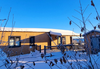 Cabaña de madera nevada en Chalet Waldfee, Camping & Ferienpark Brilon, Alemania, rodeada de ramas invernales.