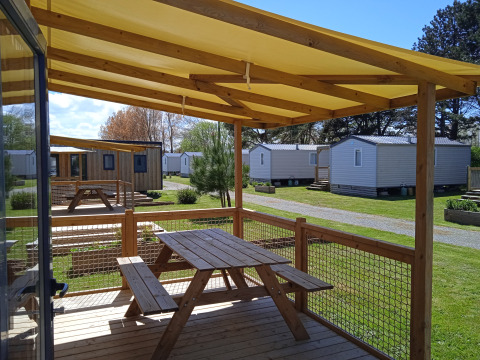 Terraza de madera con mesa y bancos en Cottage Prestige, Camping Seasonova Etennemare, Francia, cabañas alrededor.