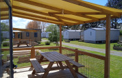 Terraza de madera con mesa y bancos en Cottage Prestige, Camping Seasonova Etennemare, Francia, cabañas alrededor.
