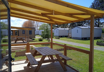 Overdekt houten terras met picknickbank bij Cottage Prestige, Camping Seasonova Etennemare in Frankrijk, chalets zichtbaar.