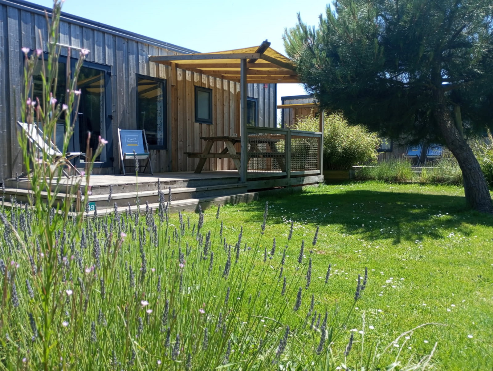 Cottage Prestige lodge bij Camping Seasonova Etennemare in Frankrijk, met houten terras en groene tuin.
