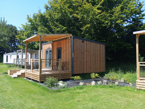 Prestige Cottage at Camping Seasonova Etennemare, France, wooden lodge with covered deck and green lawn.