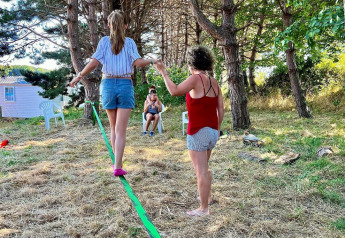 Twee vrouwen balanceren op een slackline bij Camping Seasonova Etennemare in Frankrijk onder de bomen.
