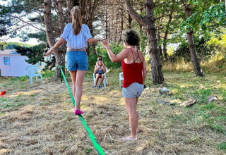 To kvinder balancerer på en slackline under træer ved Camping Seasonova Etennemare, Frankrig.