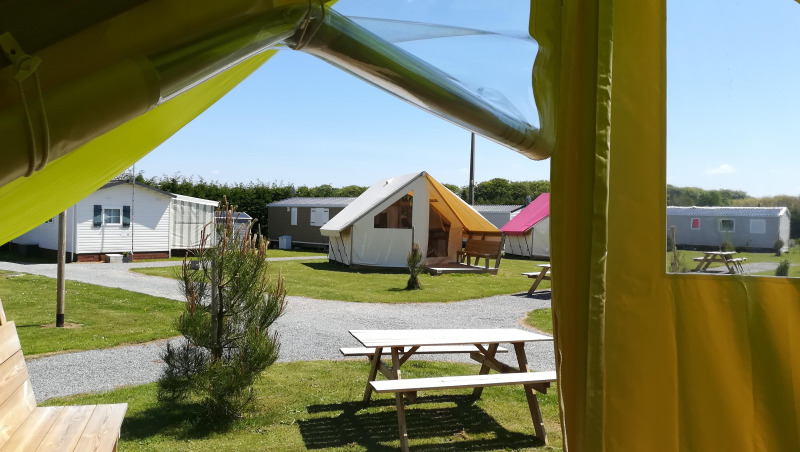 View from a safari tent Ecolodge Junior with picnic tables and other tents at Camping Seasonova Etennemare, France.
