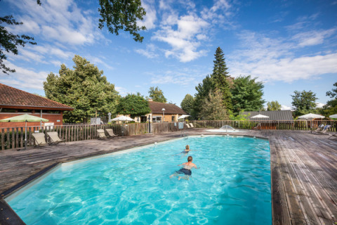Piscina exterior con niños, tumbonas y sombrillas en Camping de l'Ill - Colmar, en Grand Est, Francia.