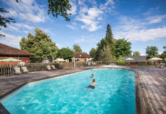 Piscina exterior con niños, tumbonas y sombrillas en Camping de l'Ill - Colmar, en Grand Est, Francia.