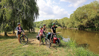 Cuatro ciclistas descansan junto a un río rodeado de árboles en Camping de l'Ill - Colmar, Francia.
